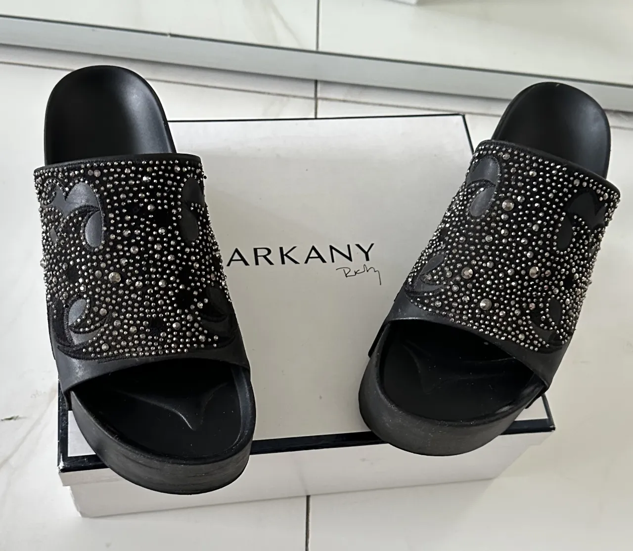 Ojotas negras con plataforma, tiras anchas adornadas con tachas plateadas y diseño grabado.