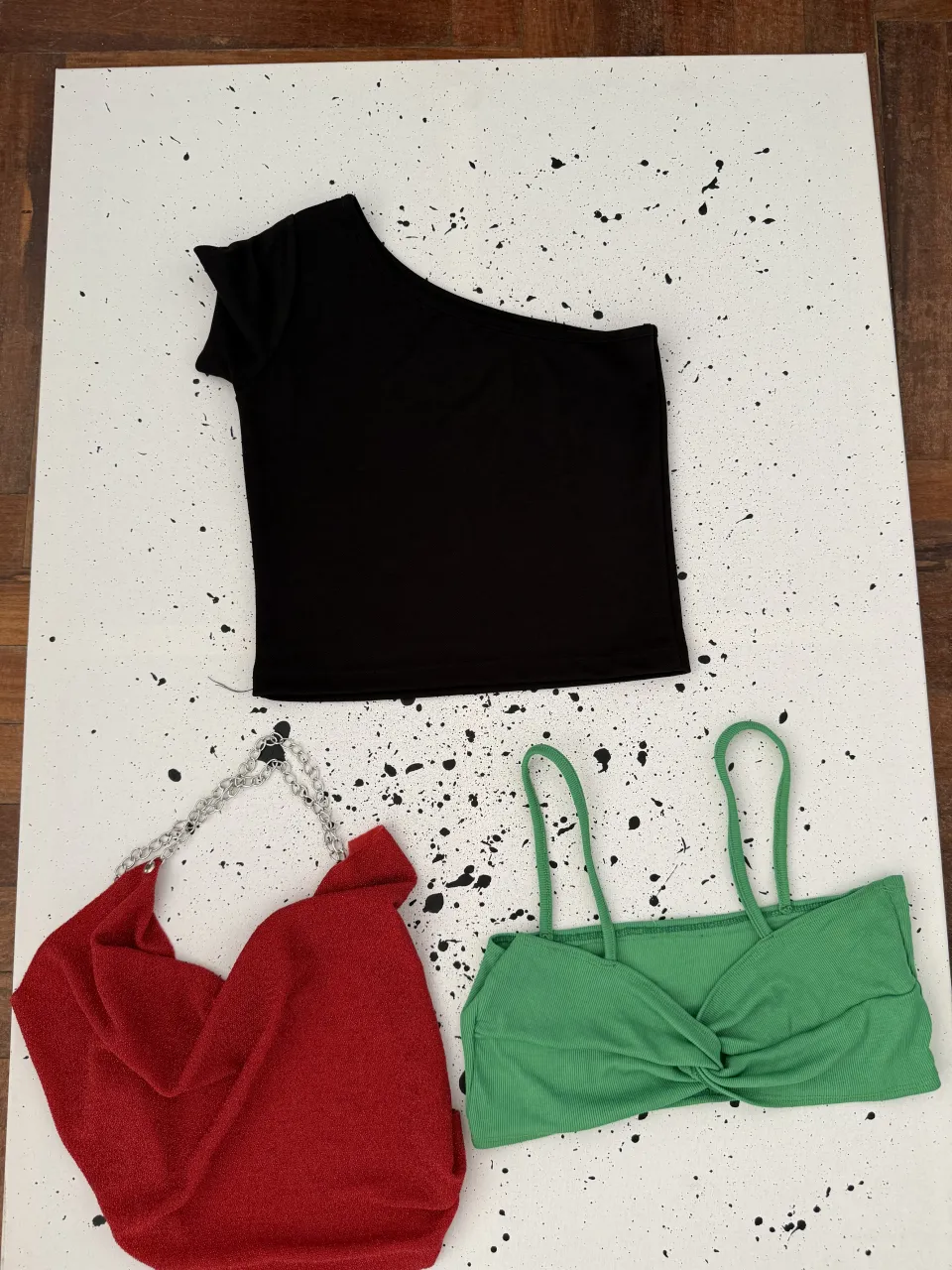 Top negro asimétrico de manga corta. Bolso rojo con cadena plateada. Top verde con tiras finas y nudo en el frente.