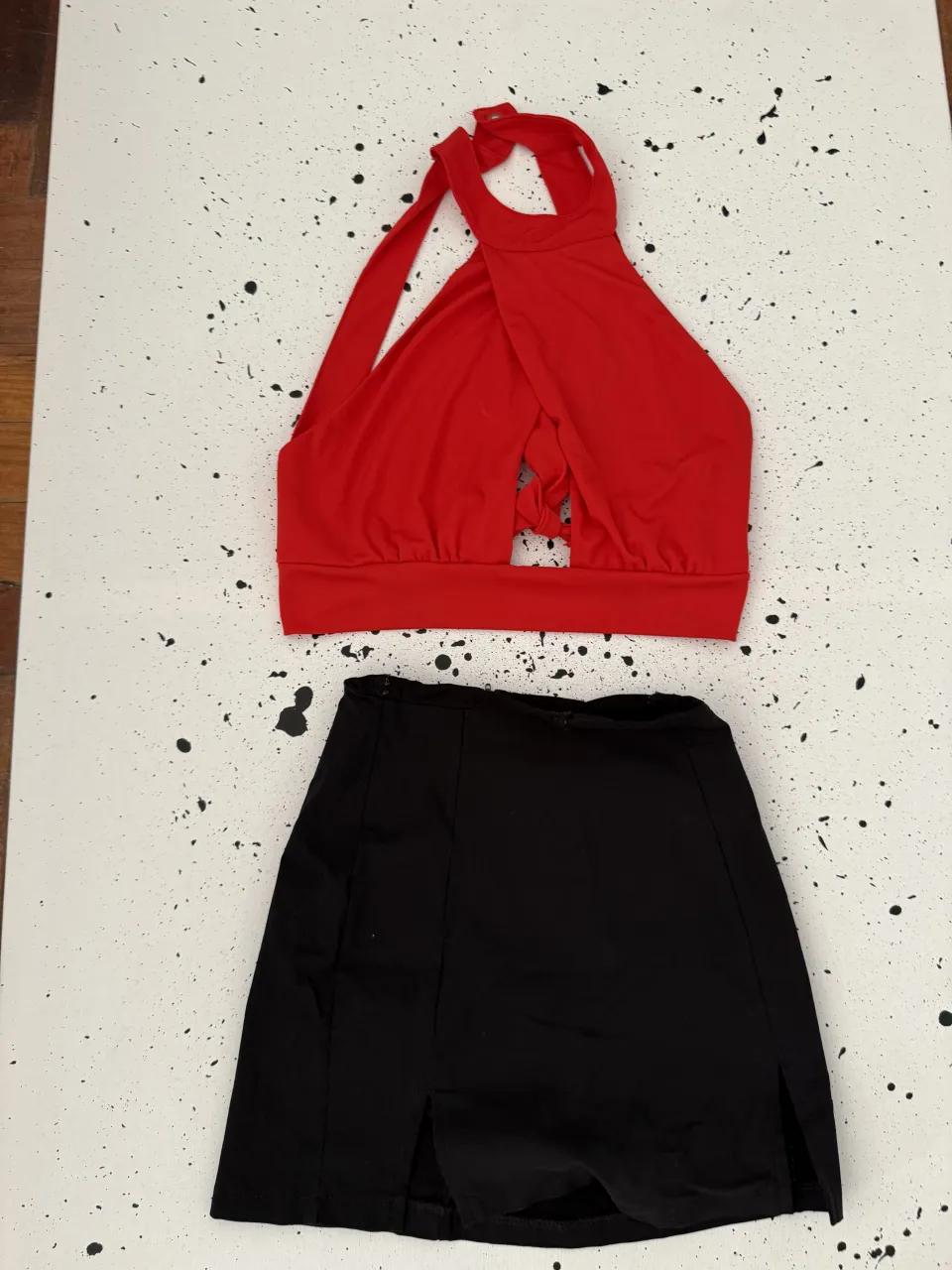 Conjunto de top rojo y pollera negra. El top es de cuello halter con tiras cruzadas en el frente y escote pronunciado. La pollera es corta con tajos laterales.