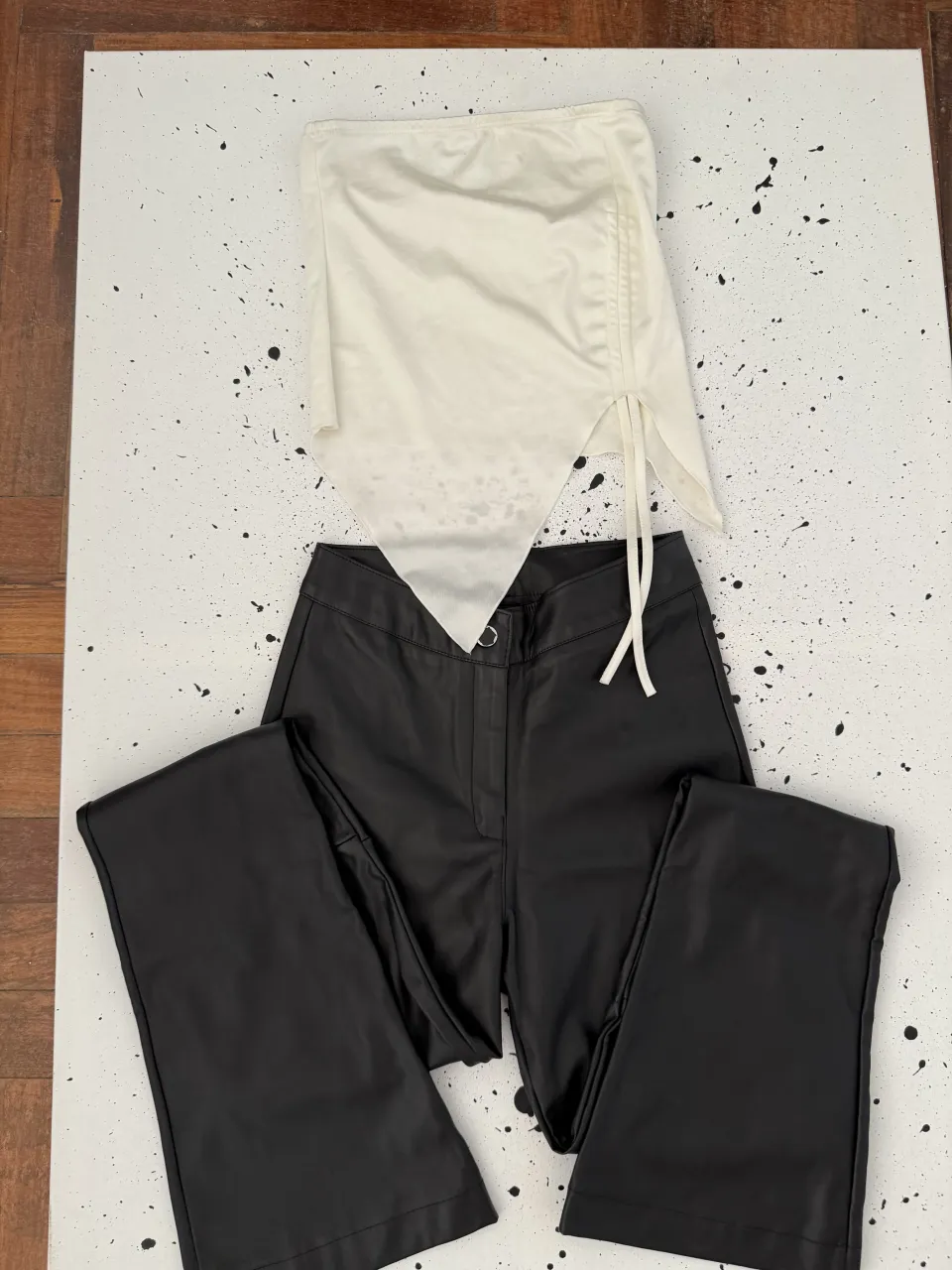 Conjunto de top blanco asimétrico con cordón lateral y pantalón negro de cuero sintético.