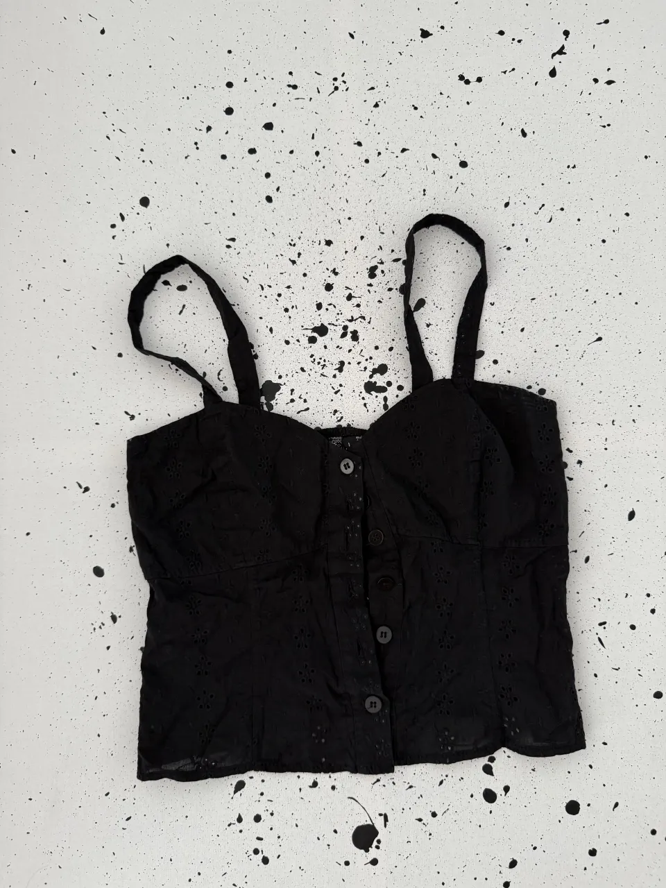 Top negro con botones al frente y breteles finos. Posee detalles de bordado calado en toda la prenda.