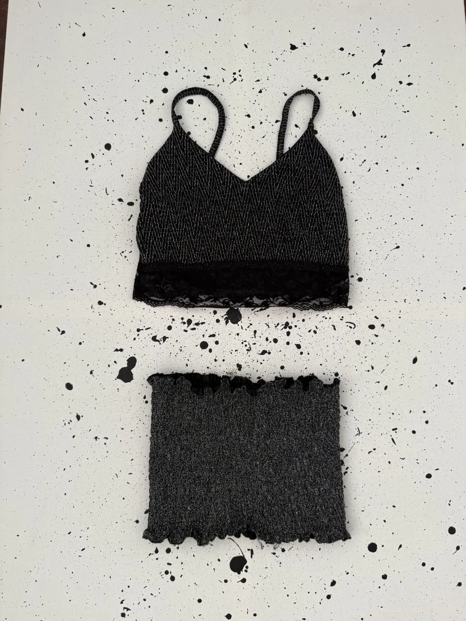 Conjunto de dos piezas: un top negro con tiras finas y detalles plateados, y un short negro con borde fruncido.