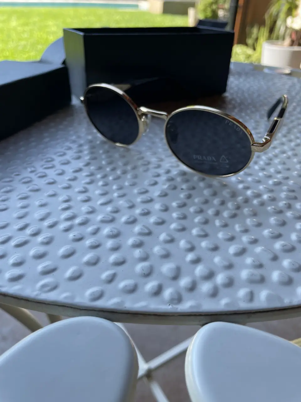 Anteojos de sol Prada, con marco dorado y lentes oscuros. Incluye estuche y paño de limpieza.