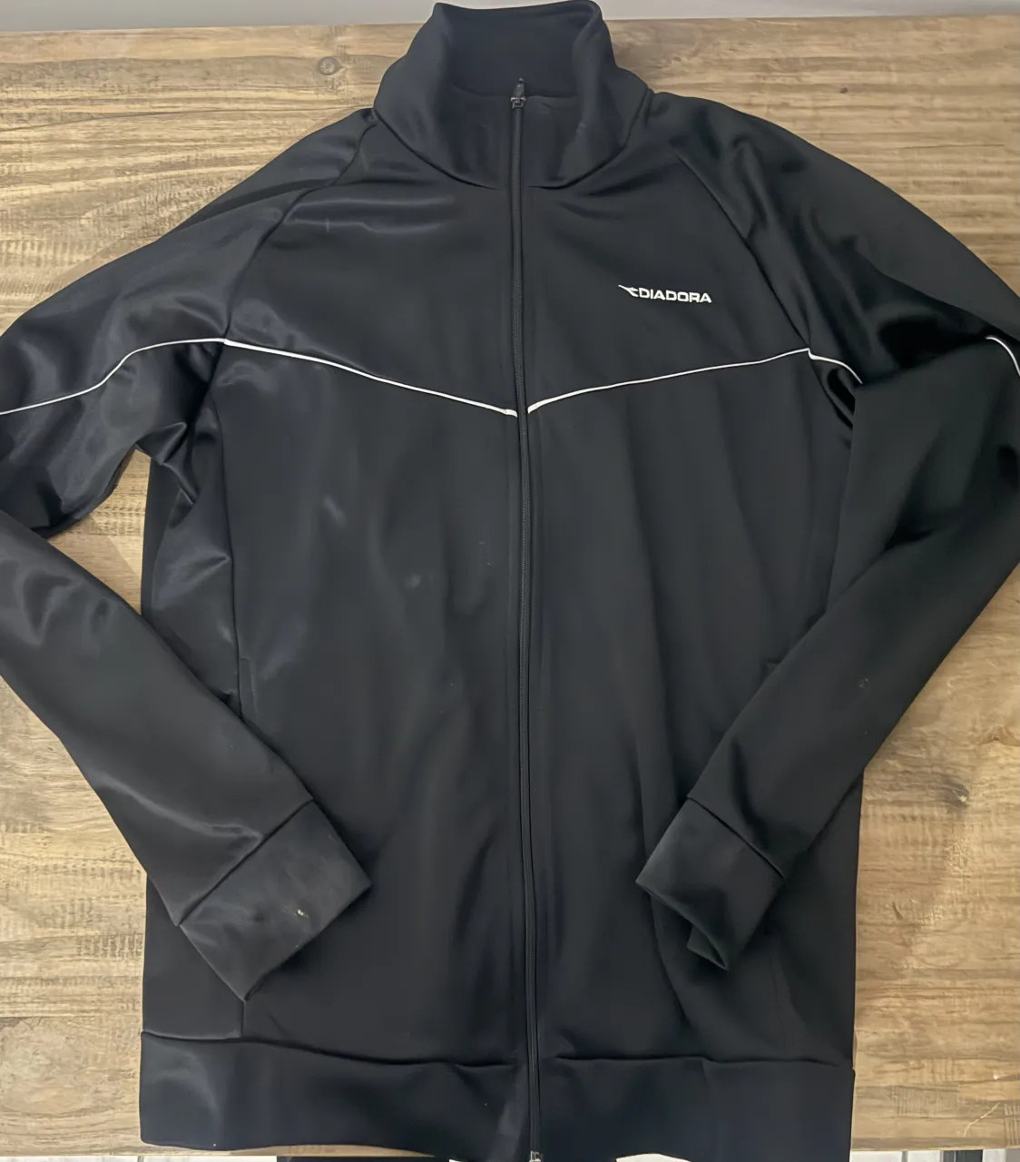 Buzo deportivo negro con cierre completo y detalles de líneas blancas en el frente y mangas. Cuello alto.