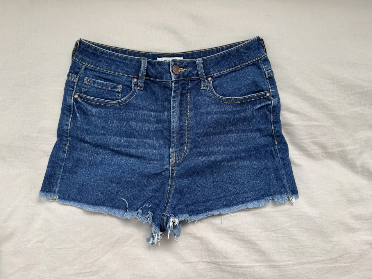 Short tiro alto de jean azul con deshilachados en el borde inferior. Muy elastizado.