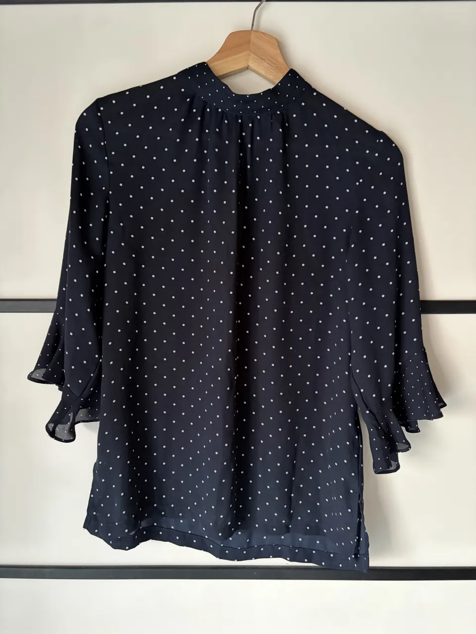 Blusa azul marino con lunares blancos y mangas acampanadas con volados. Cuello alto con detalle de botones en la espalda.