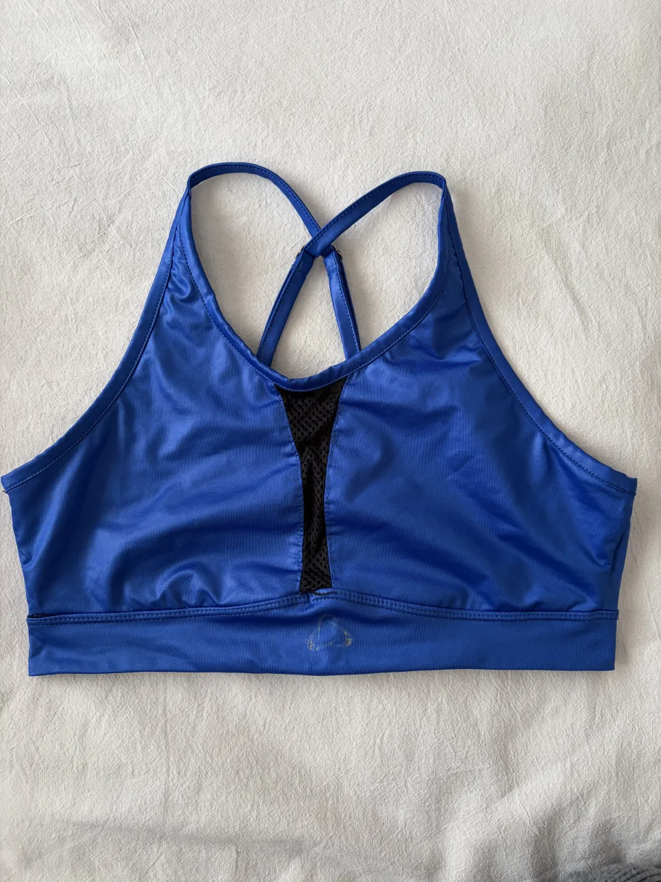 Top deportivo azul con detalles de red negra en el frente y tiras cruzadas en la espalda. Posee logo plateado en la parte inferior del frente y en la espalda.