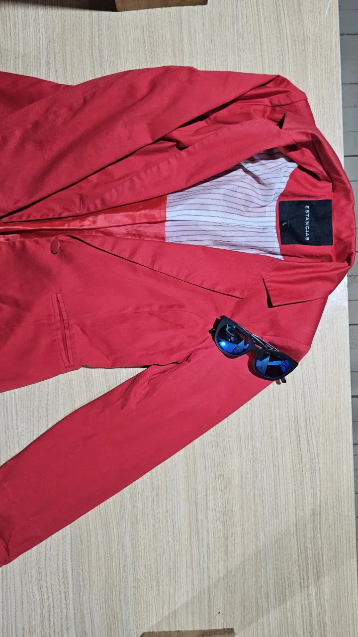 Blazer rojo con un botón al frente y bolsillos con solapa. El forro interior es a rayas blancas y negras.