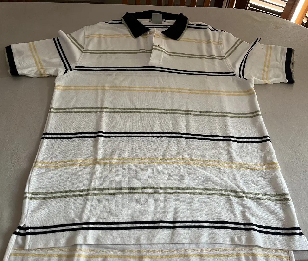 Remera polo de hombre, blanca con rayas horizontales en amarillo, verde y negro. Cuello y terminaciones de mangas en negro. Talle XL.