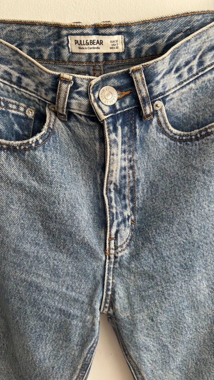 Jeans tiro alto con roturas en los tobillos. Cierre con botón y bolsillos delanteros y traseros.