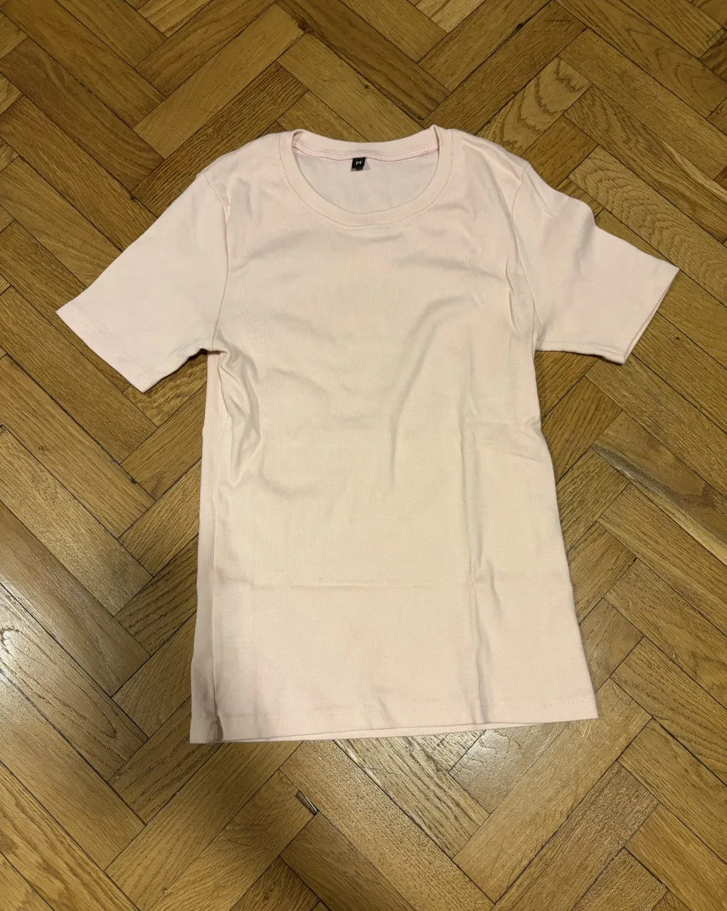 Remera de manga corta y cuello redondo, de color rosa pálido. Posee una textura acanalada. 100% algodon