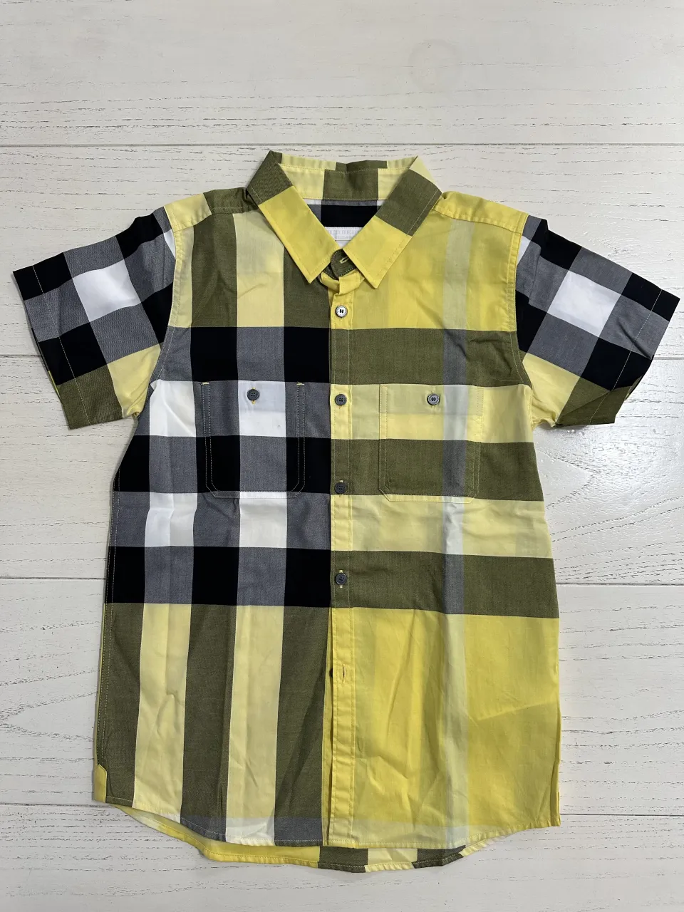 Camisa a cuadros manga corta, con botones al frente y dos bolsillos en el pecho. Cuello clásico.