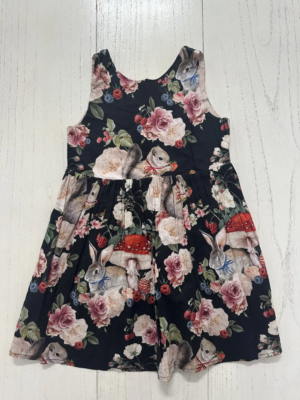 Vestido negro con estampado de conejos, ardillas, flores y hongos. Diseño sin mangas y con cuello redondo.