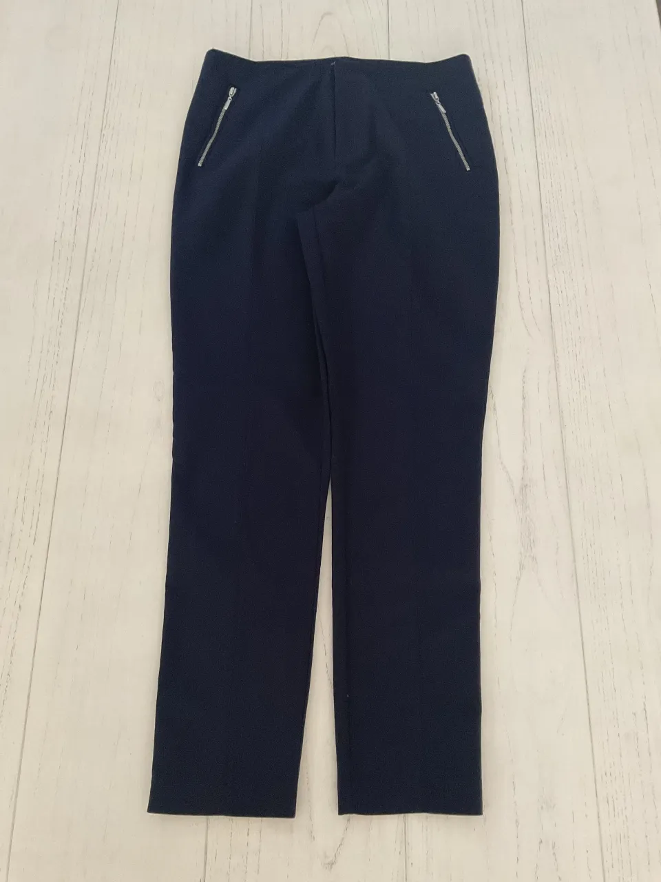 Pantalón de vestir azul marino, tiro alto, con detalles de cierres plateados en los bolsillos delanteros y una fina línea blanca lateral en cada pierna. Ideal para un look elegante y moderno.