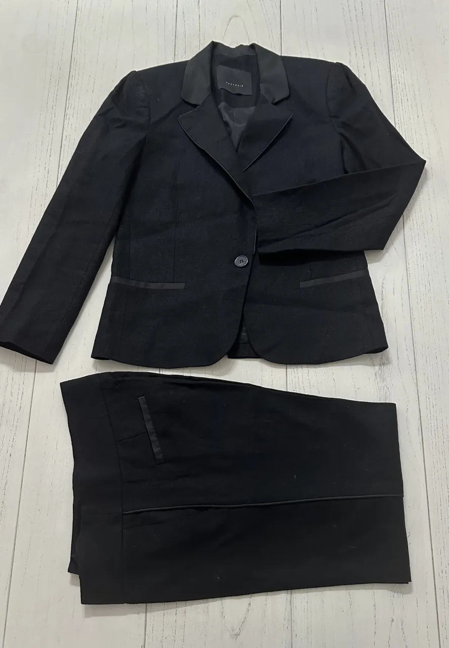 Conjunto de saco y pantalón negro. El saco tiene un botón al frente y solapas.