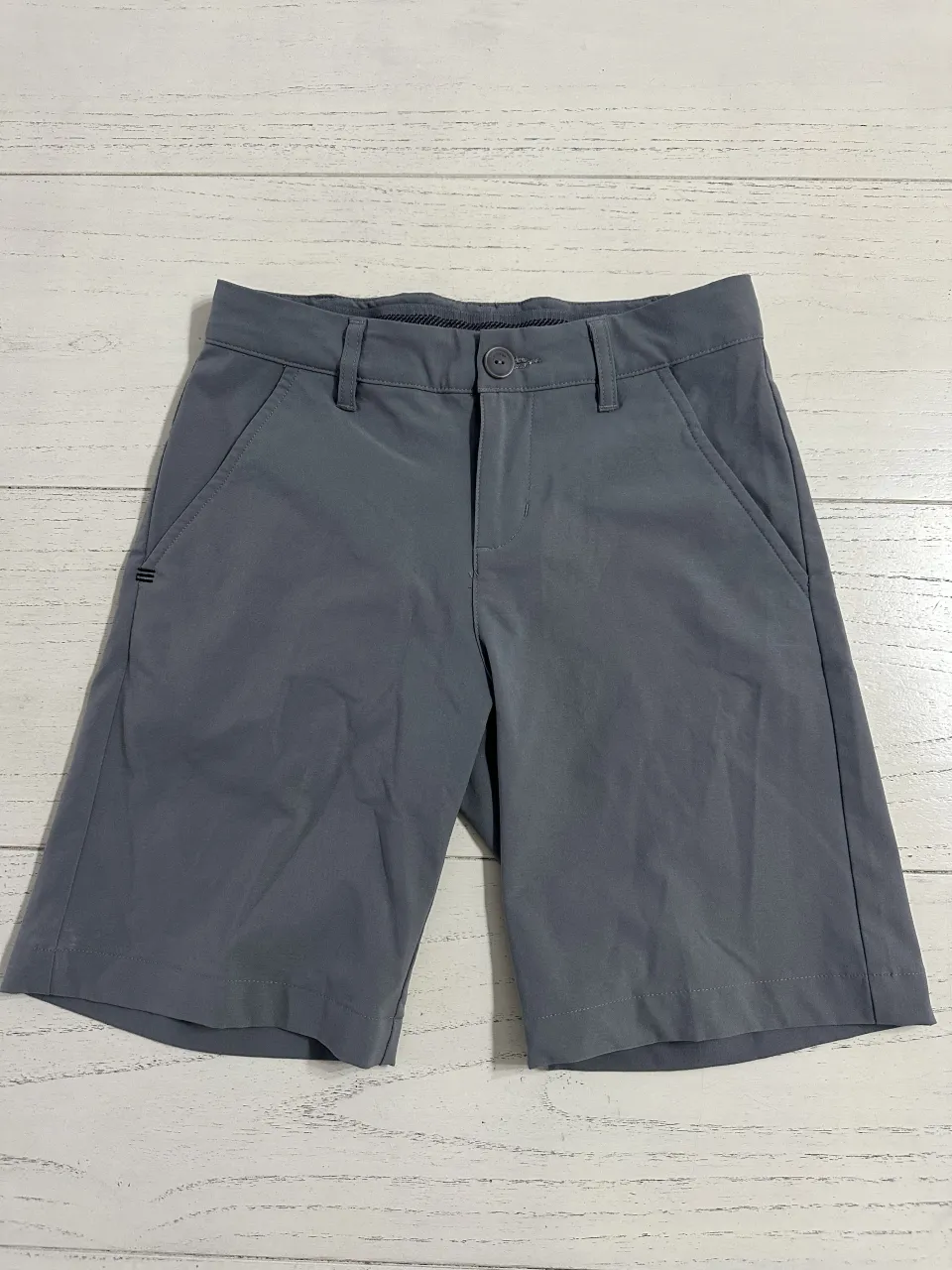 Shorts de vestir grises con cierre y botón. Tienen bolsillos delanteros y uno trasero.