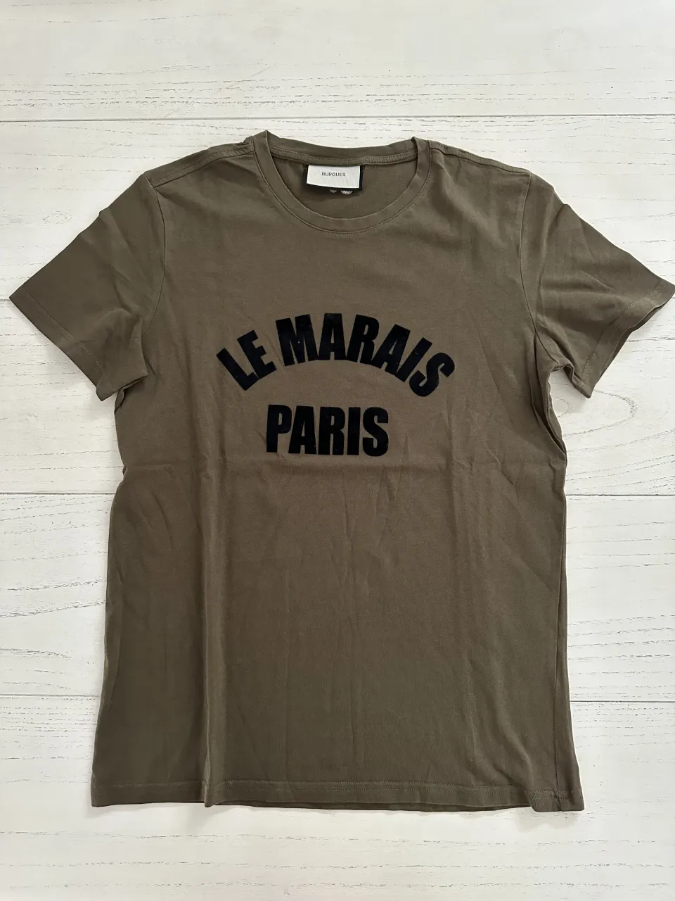 Remera de algodón color verde militar con estampa "LE MARAIS PARIS" en negro. Cuello redondo y manga corta. Ideal para un look casual y urbano.