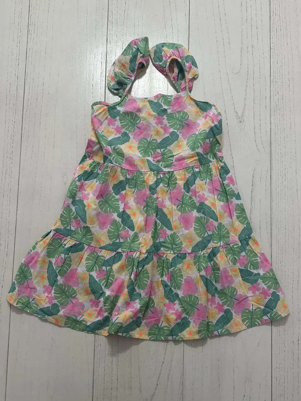Vestido estampado de flores tropicales en tonos verdes, rosas y amarillos. Posee tirantes finos y volados en los hombros. La parte superior es fruncida con elástico.