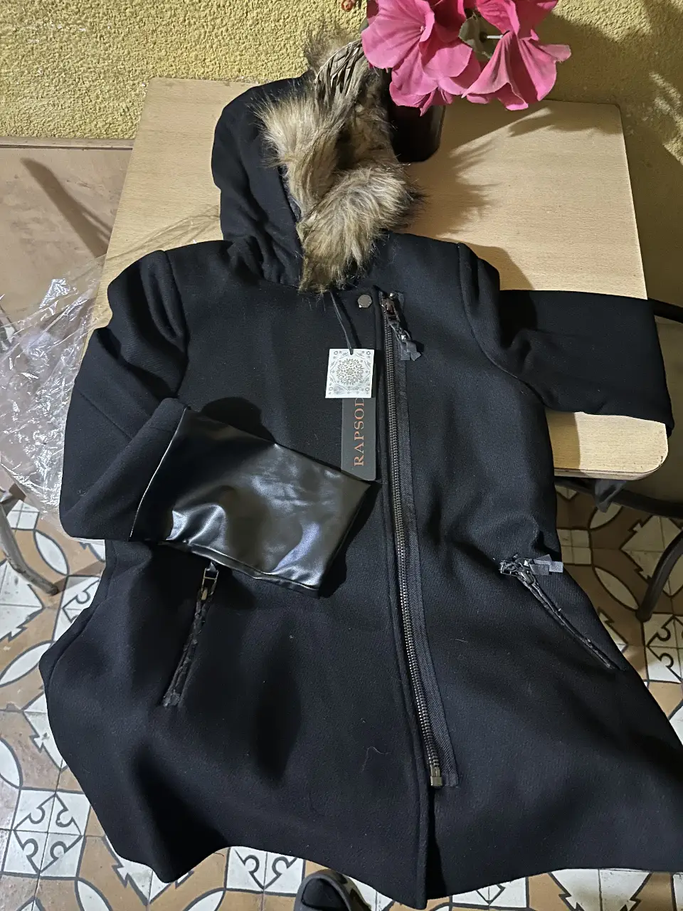 Tapado negro de mujer, con capucha con borde de piel sintética, cierre frontal y detalles de cuero en las mangas. Ideal para el invierno.