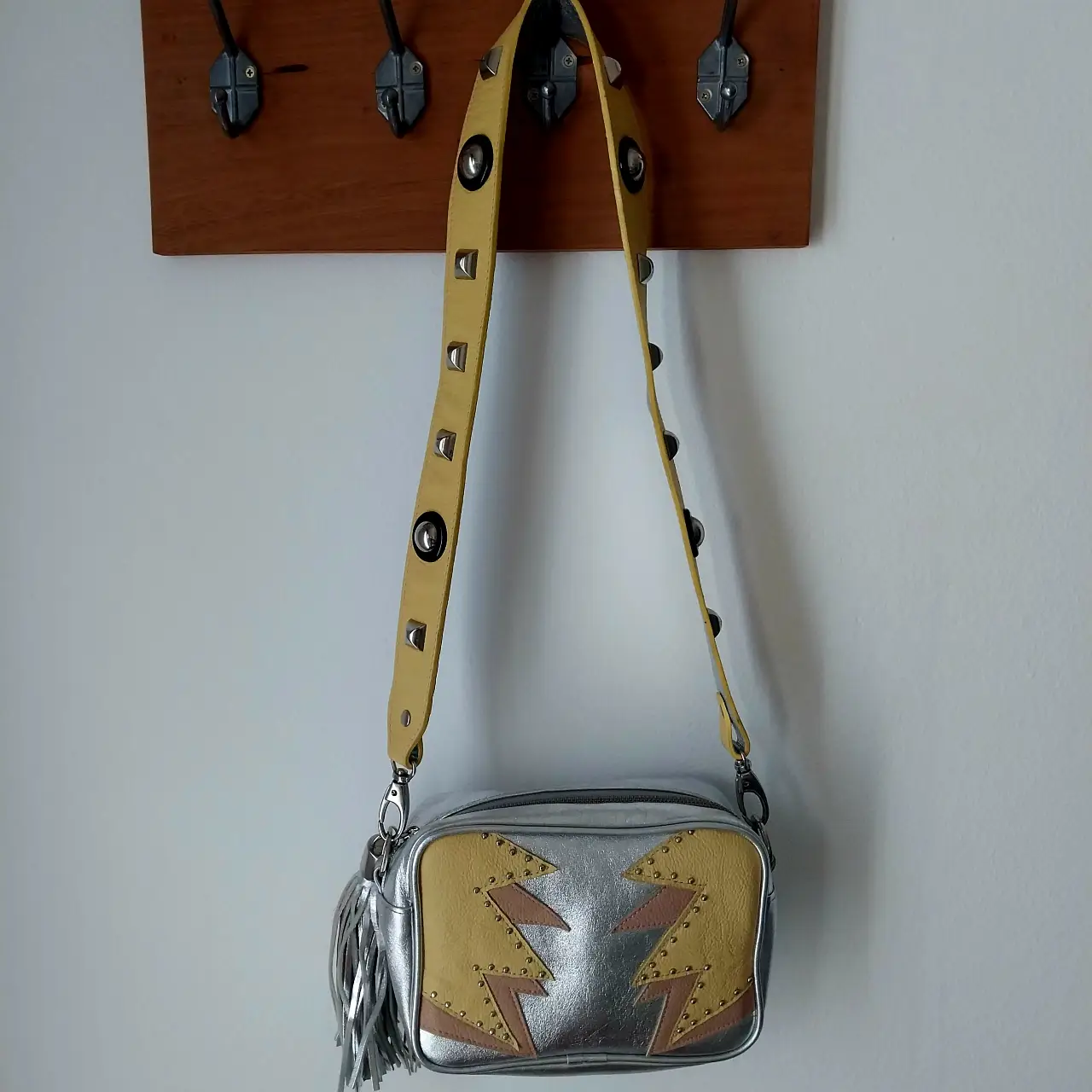 Cartera bandolera Desiderata con diseño de rayos en amarillo y plateado, detalles de tachas y flecos. Ideal para un look rocker y canchero.