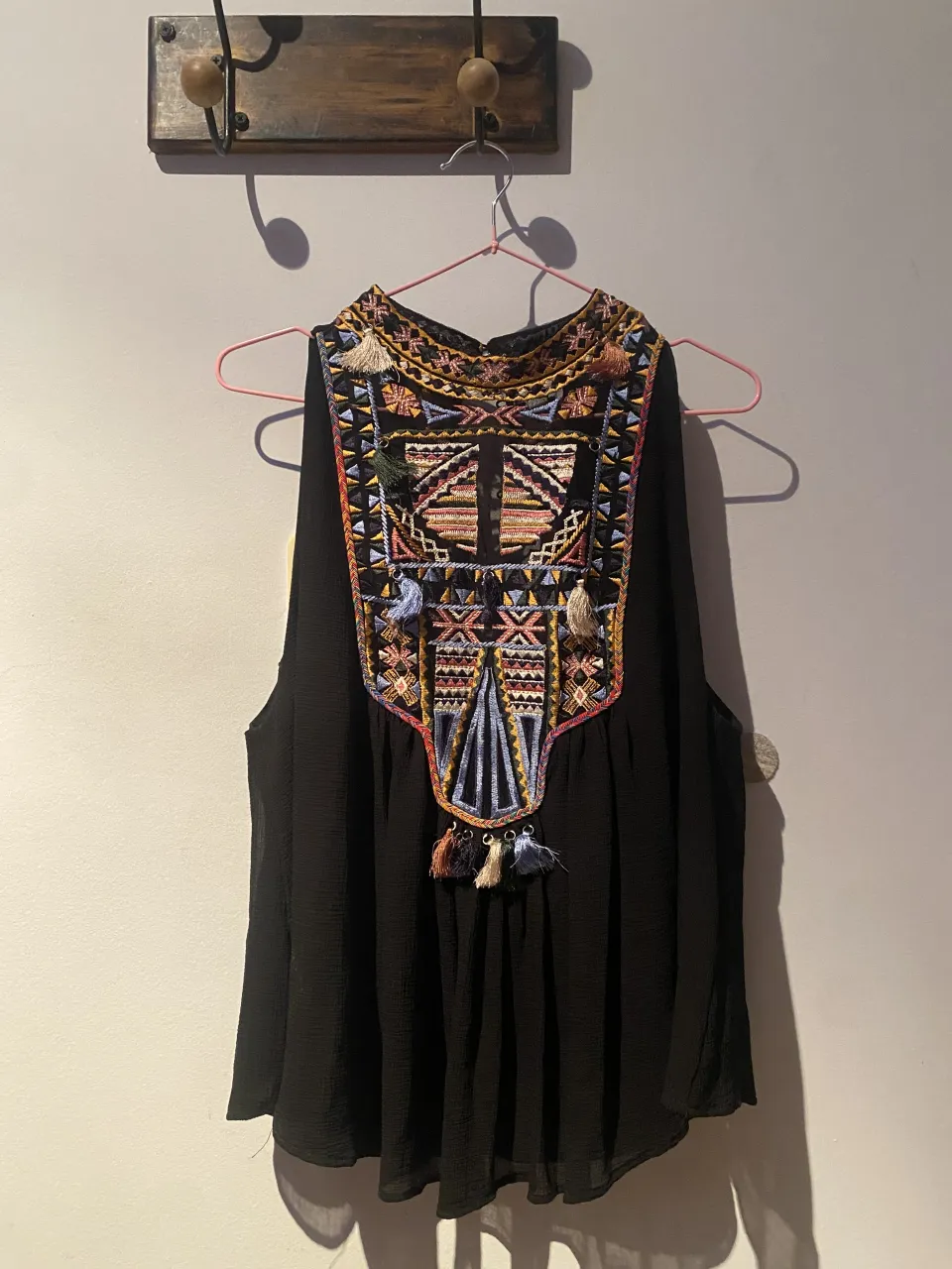 Musculosa negra con cuello alto y bordado de estilo étnico en el frente. El bordado es multicolor con detalles de flecos y tiene un par de botones en la parte superior de la espalda.