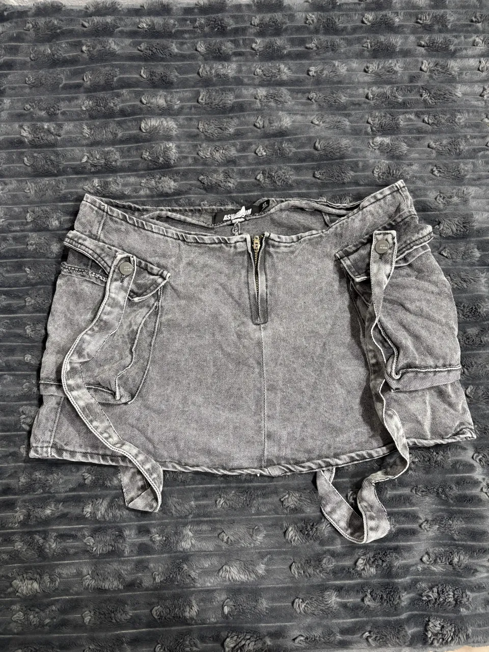 Pollera de jean gris con detalles de tiras y bolsillos cargo. Cierre delantero.