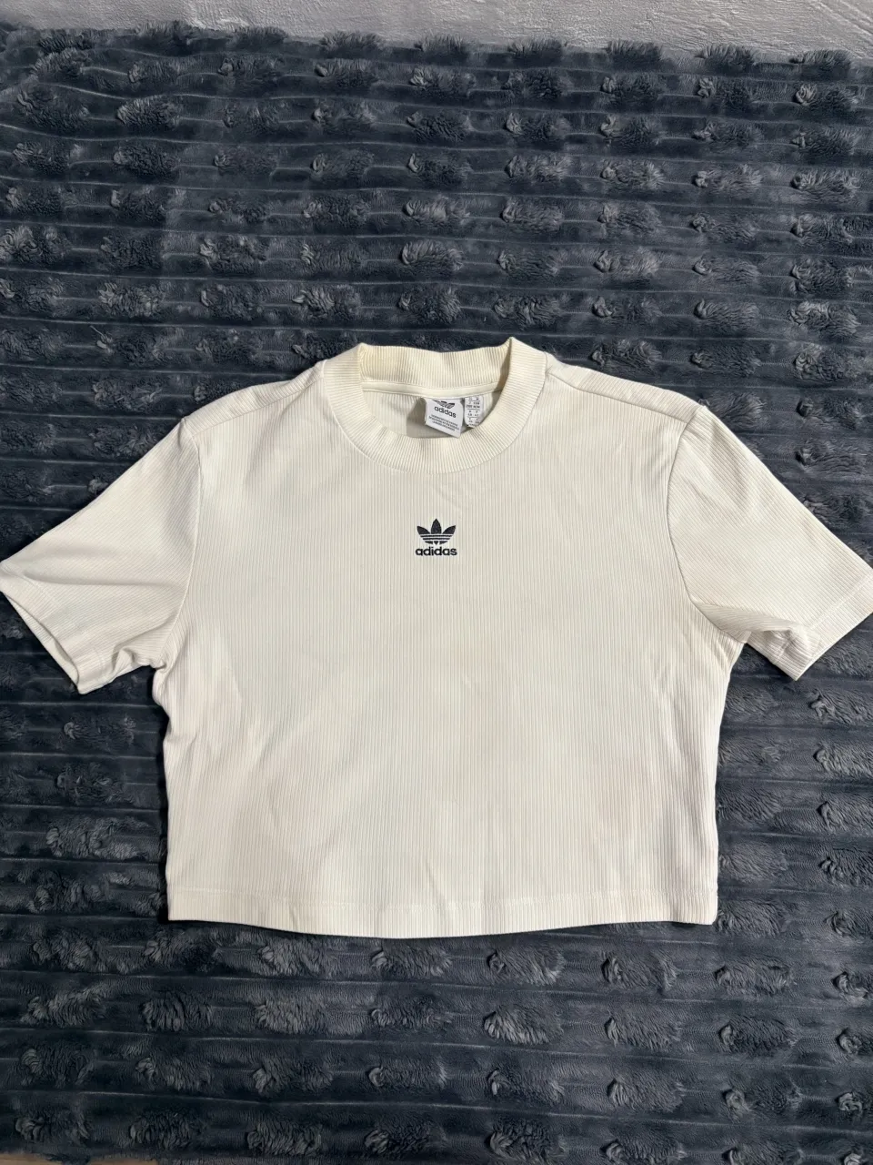 Remera blanca de algodón acanalado con logo de Adidas bordado en el pecho.