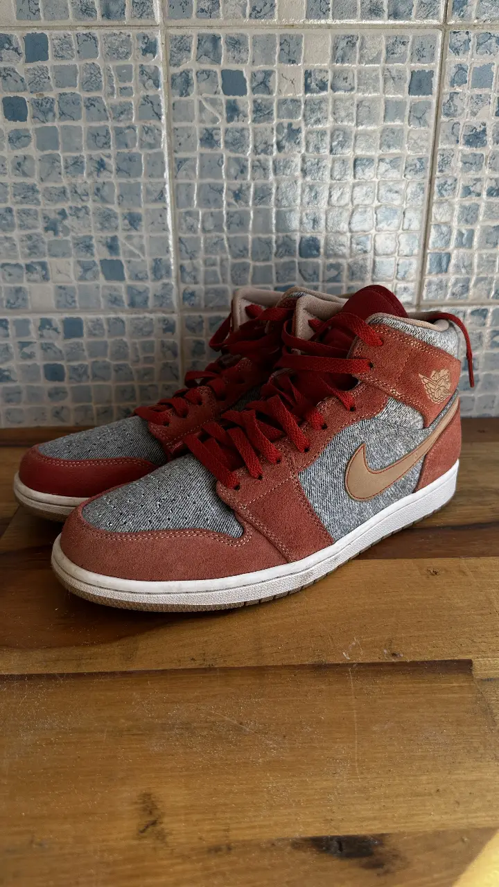 Zapatillas Air Jordan 1 Mid, con detalles en rojo y gris. Diseño icónico y estilo urbano para un look auténtico.