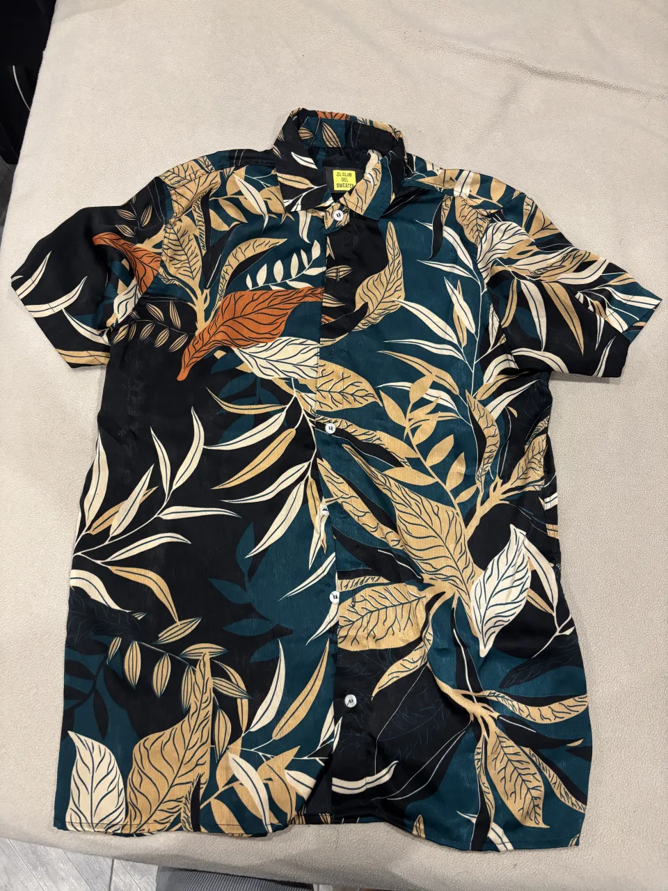 Conjunto estampada con hojas y flores en tonos verdes, negros, dorados y naranjas. Posee cuello camisero y botones al frente.