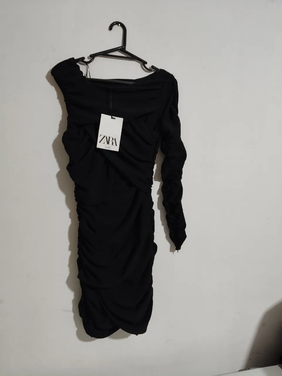 Vestido negro de fiesta con un solo hombro y detalles de fruncido en toda la prenda. Diseño elegante y moderno, ideal para eventos especiales.