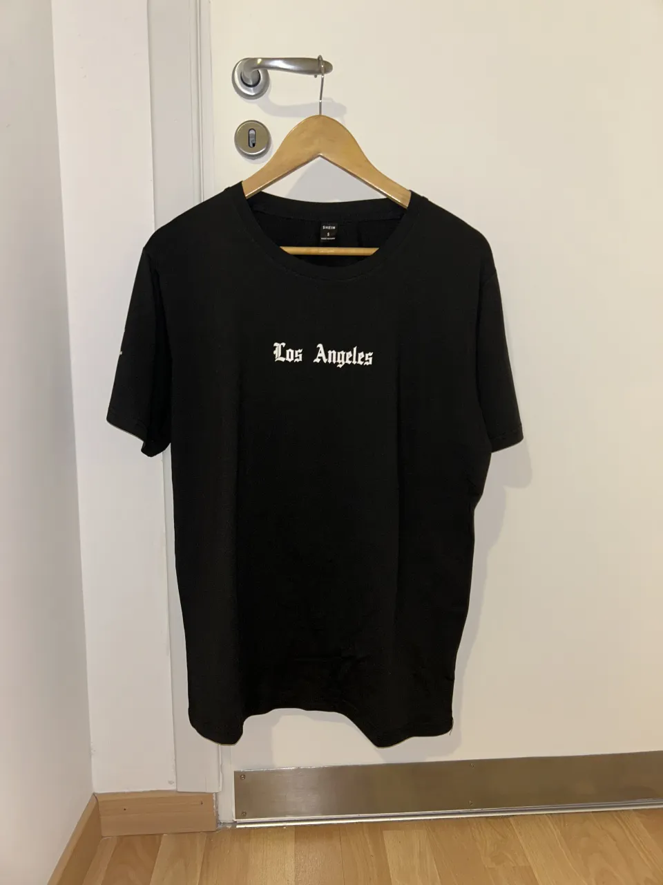 Remera negra de manga corta con estampa "Los Angeles" en la espalda y en el frente. Tiene una frase escrita en la manga.