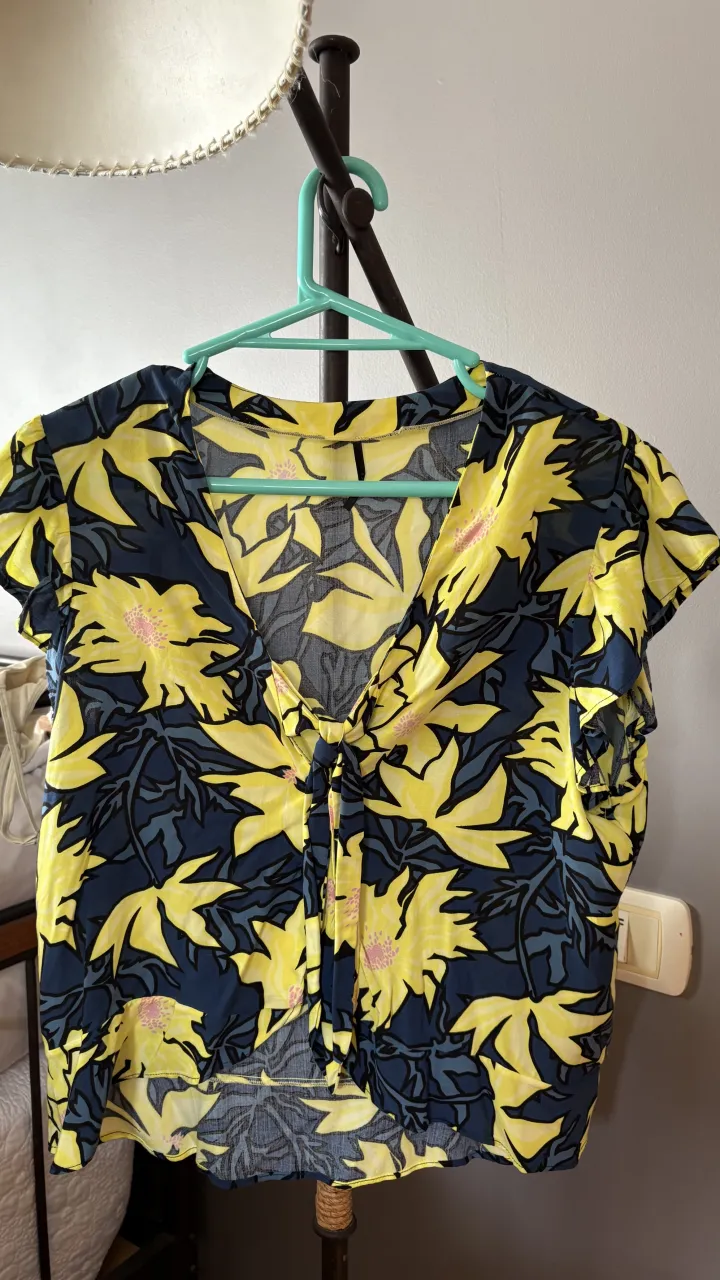 Remera amarilla con estampa de flores y hojas en azul oscuro. Posee un nudo en la parte delantera y mangas cortas con volados.
