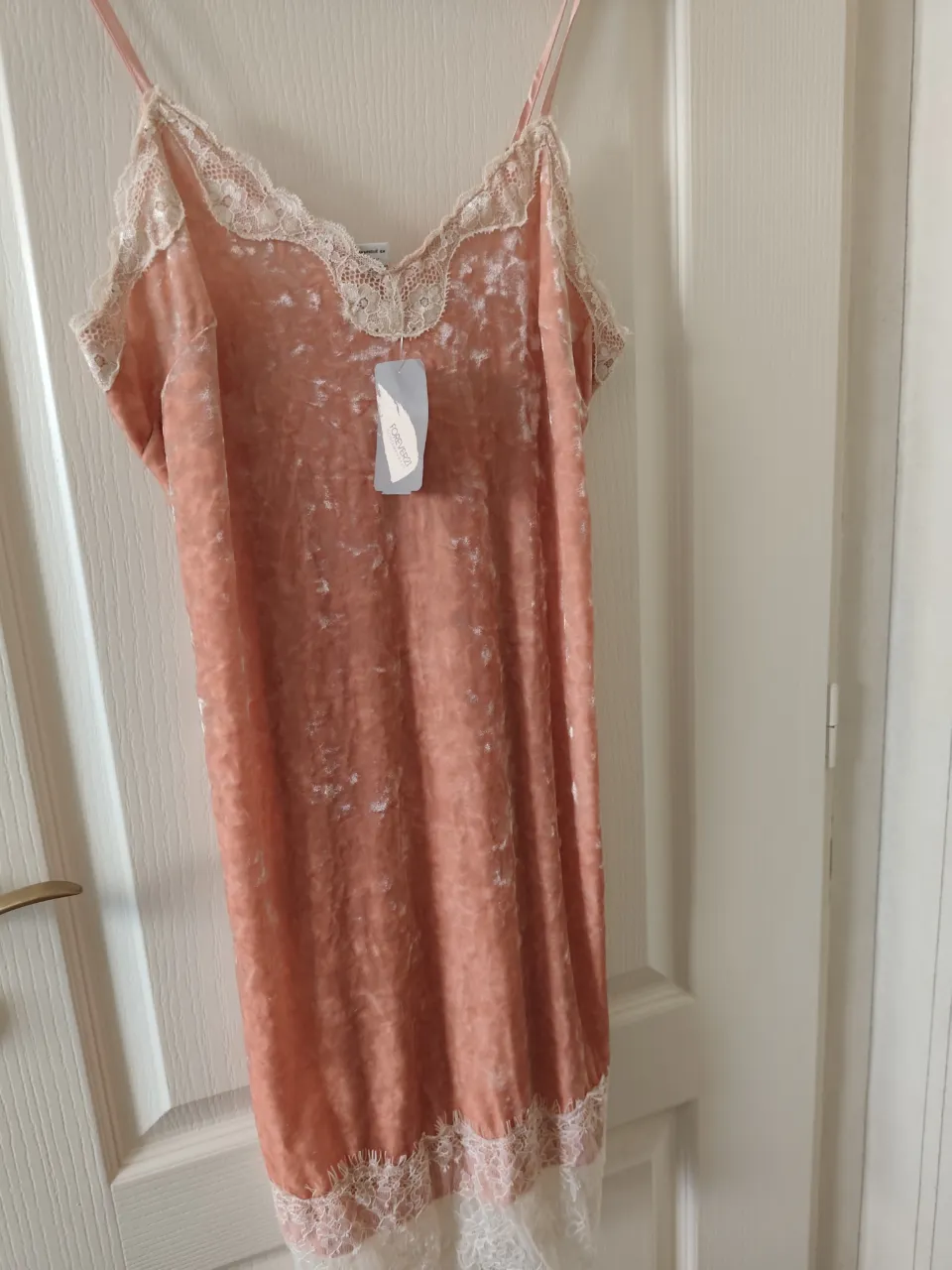 Vestido simil gamuza rosa con detalles de encaje blanco en el escote y en el borde inferior. Breteles finos regulables. El color es más parecido a un coral claro.
