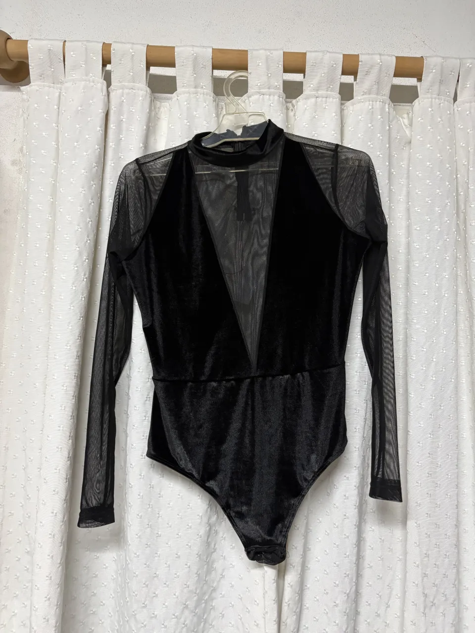 Body negro de cuello alto con cierre y mangas largas de red. Posee un escote en V pronunciado con detalles de red.