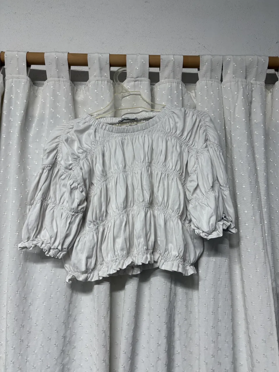 Blusa blanca con fruncido en toda la prenda y mangas abullonadas con elástico en los puños. Posee volados en el borde inferior.