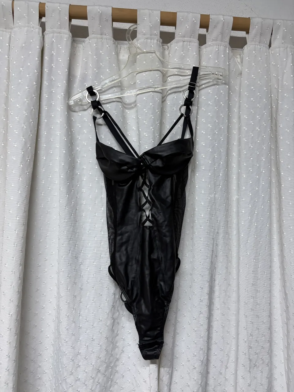 Body de cuero sintético negro con detalles de mesh y tiras cruzadas en el frente. Posee tiras finas en los hombros y aros metálicos en la parte superior y en los laterales de la cadera.