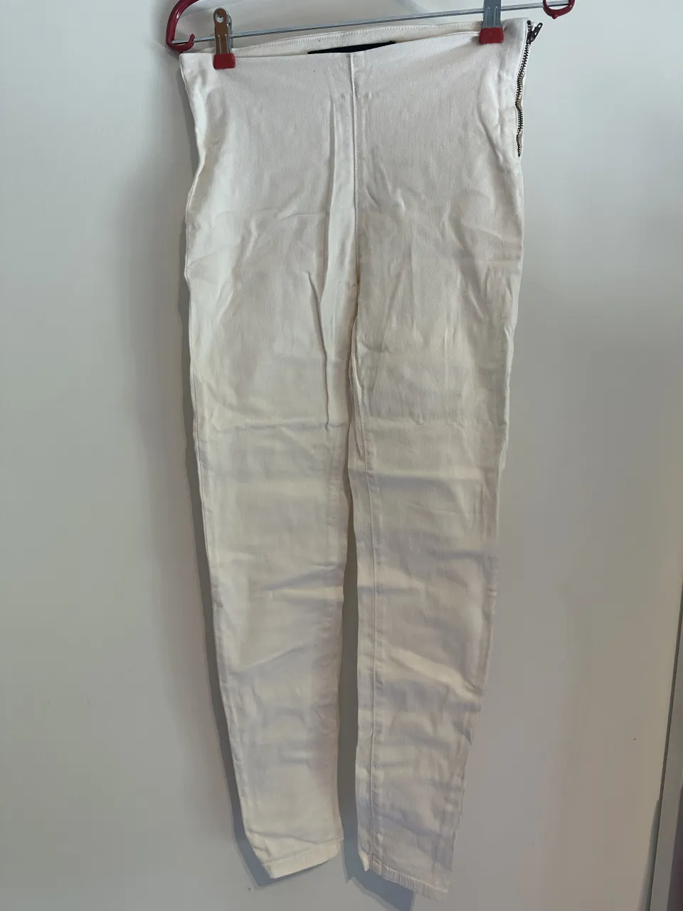 Pantalón/legging blanco tiro alto, corte chupín y con cierre metálico en el lateral. Ideal para un look casual y moderno.