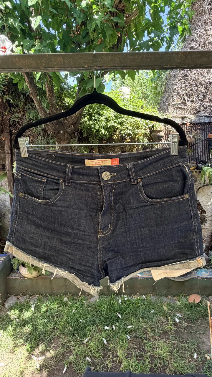 Shorts de jean elastizado, azul oscuro con detalles desflecados en los bordes inferiores. Presentan costuras a la vista en color ocre y bolsillos delanteros y traseros.