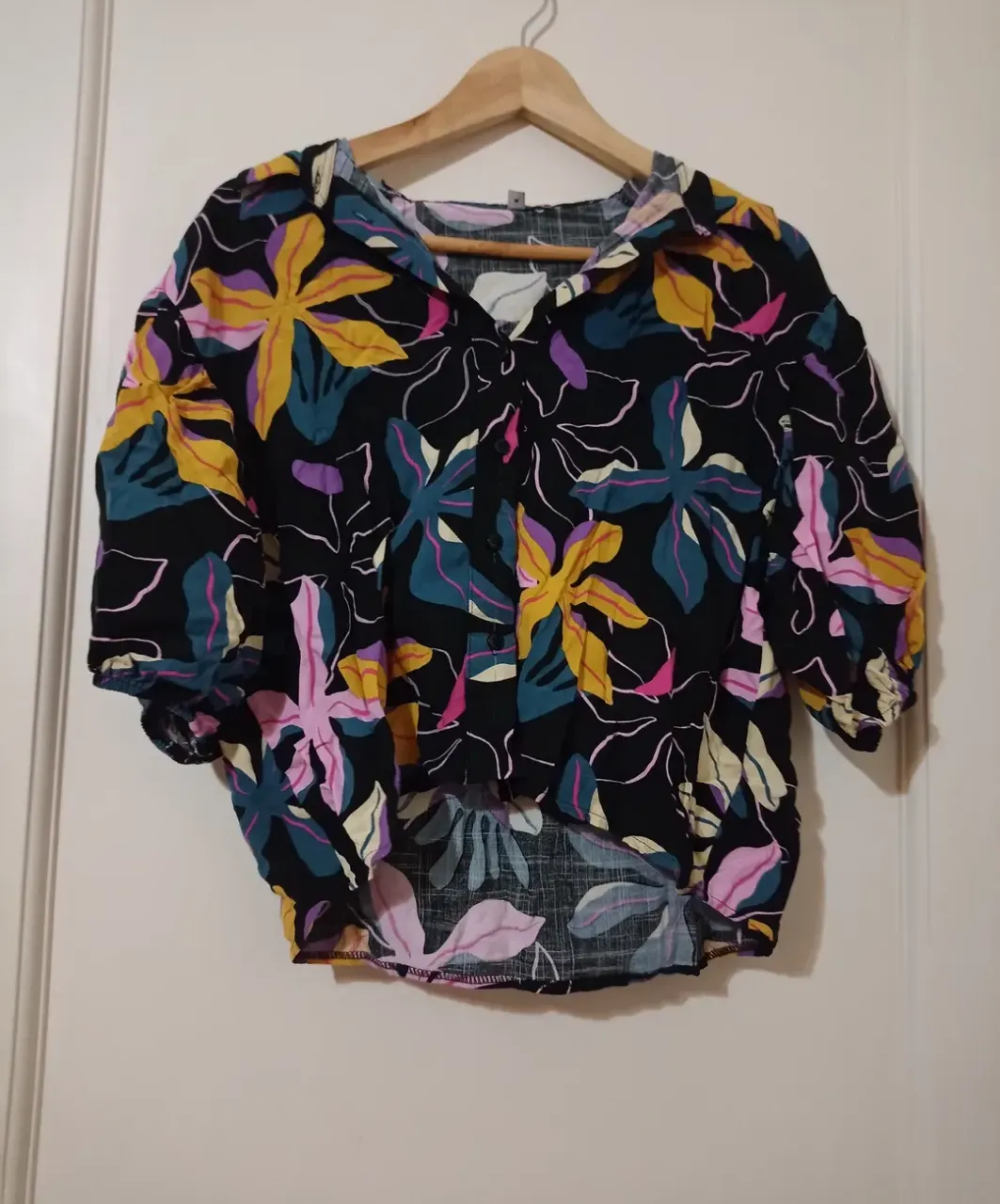 Remera estampada con flores en tonos vibrantes sobre fondo negro. Posee mangas cortas con elástico en el puño y cuello camisero.
Talle S/M 