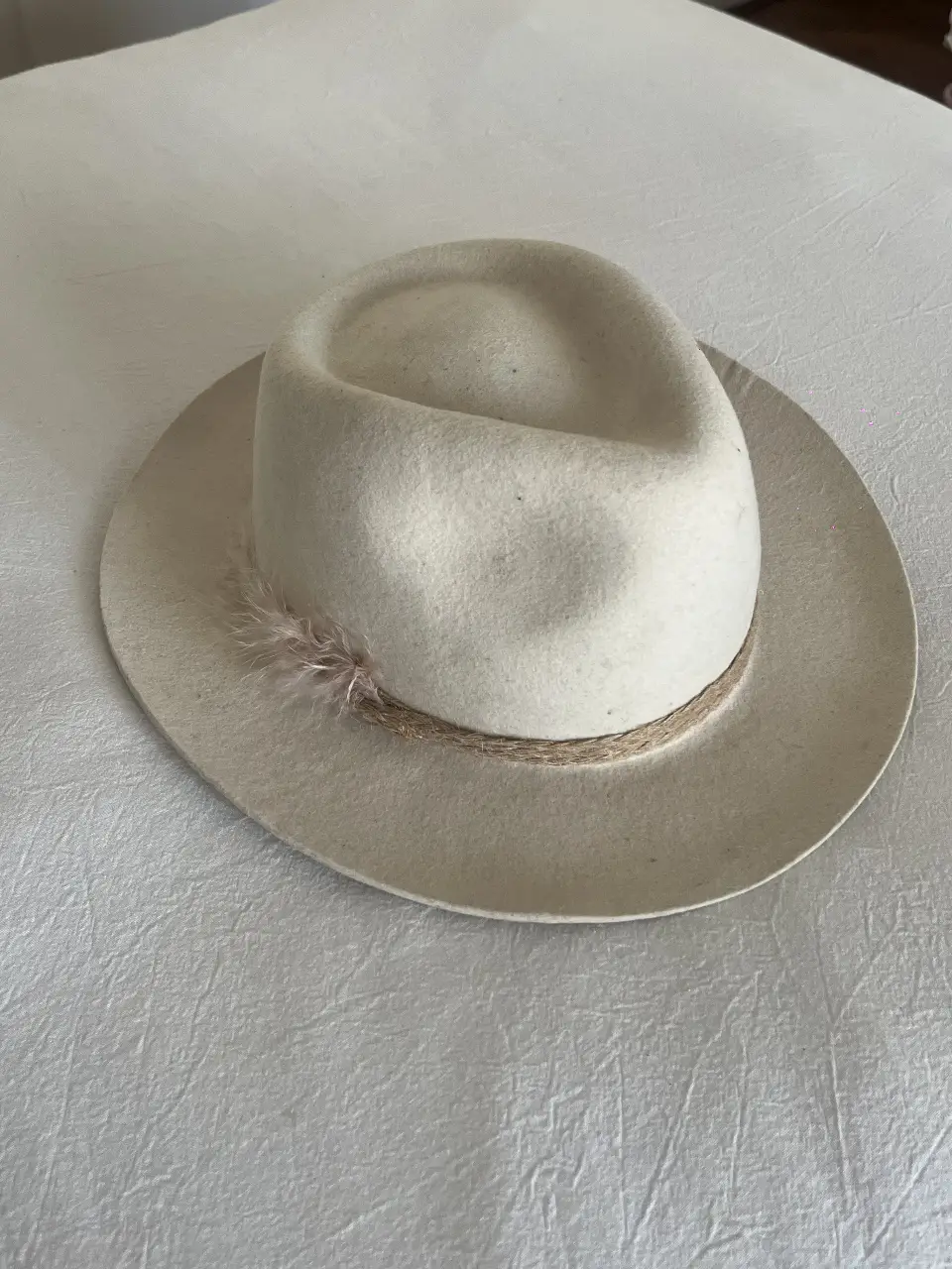 Sombrero de fieltro color crudo, con detalle de plumas rosas y cinta decorativa. Ideal para complementar cualquier look con estilo y elegancia. Circunferencia de 16cmx20cm