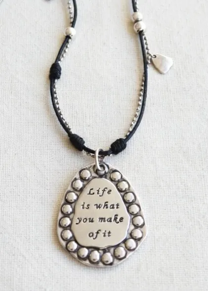 Collar con dije ovalado grabado "Life is what you make of it". Cadena con cuentas y detalles de corazones pequeños.