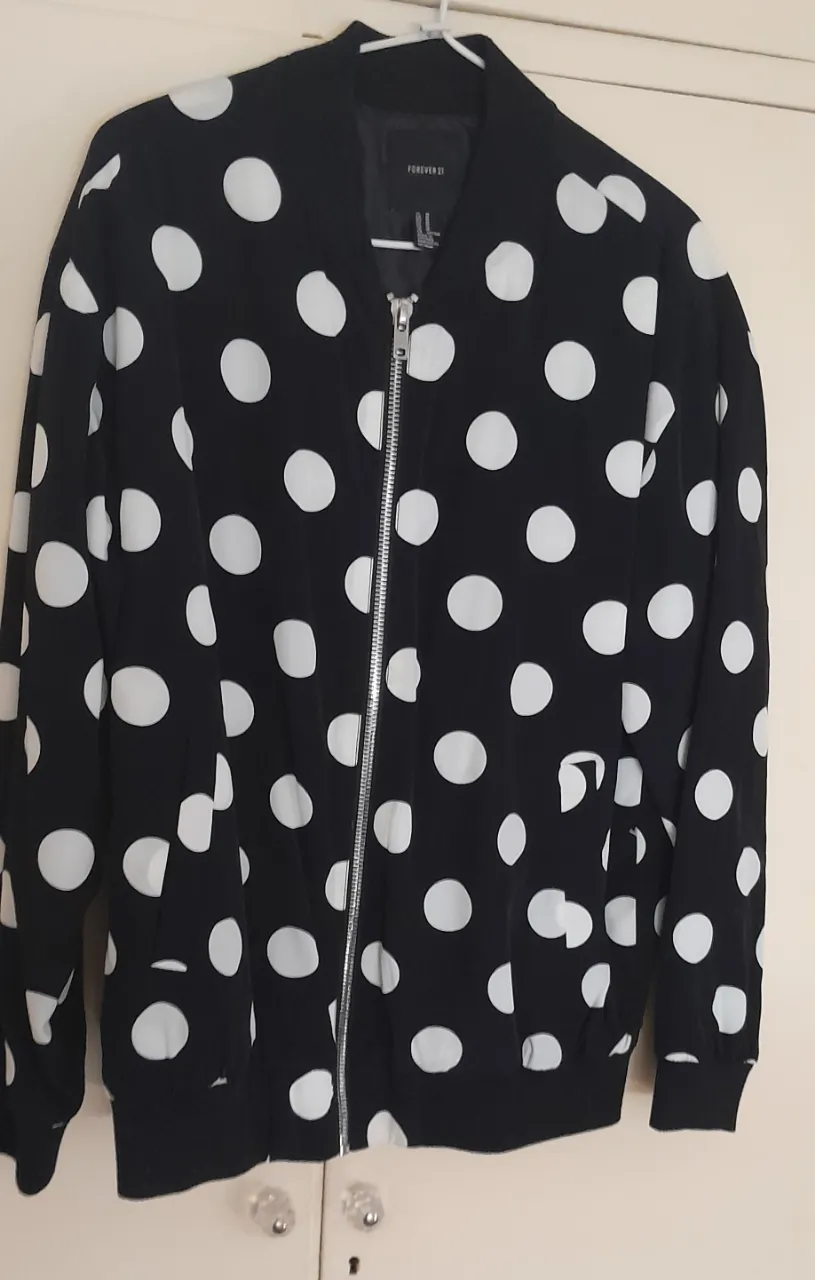 Campera bomber negra con lunares blancos. Tiene cierre metálico y bolsillos frontales.