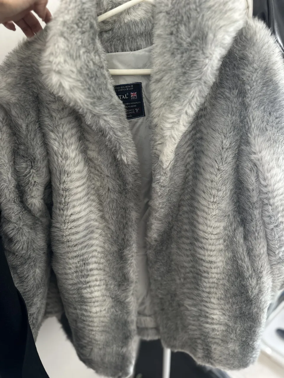 Tapado de pelo sintético gris con rayas blancas y grises. Posee cuello y se abre al frente.