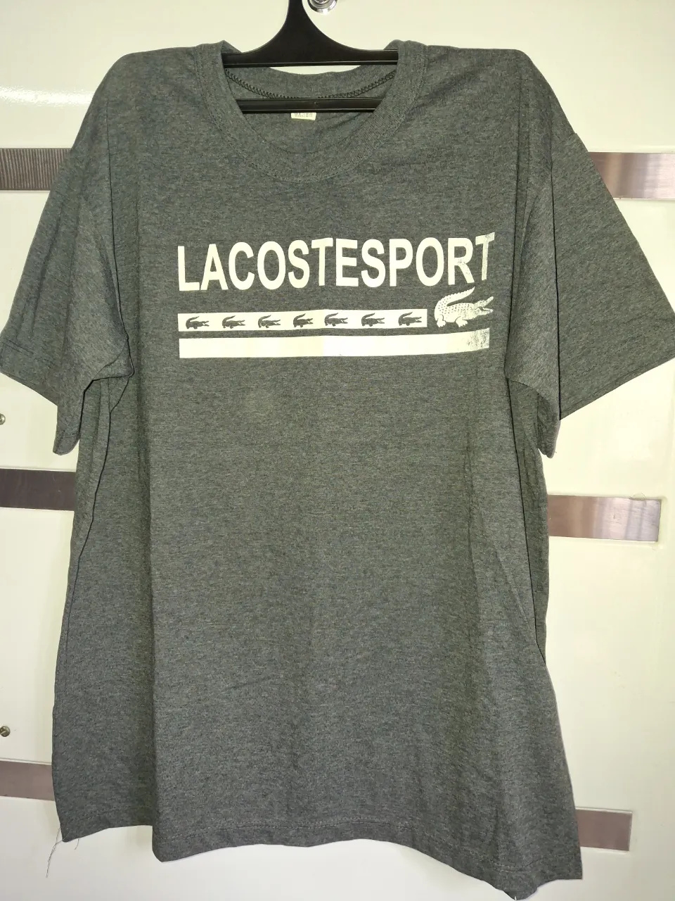 Remera gris de manga corta con estampa de "LACOSTE SPORT" en blanco y el logo de la marca.