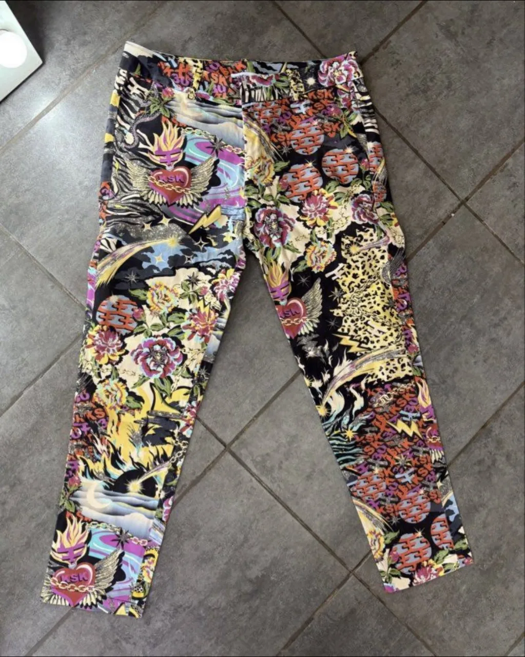 Pantalón Kosiuko estampado multicolor con diseño de corazones alados, flores, cadenas y rayos. Posee cierre y botón. casi sin uso