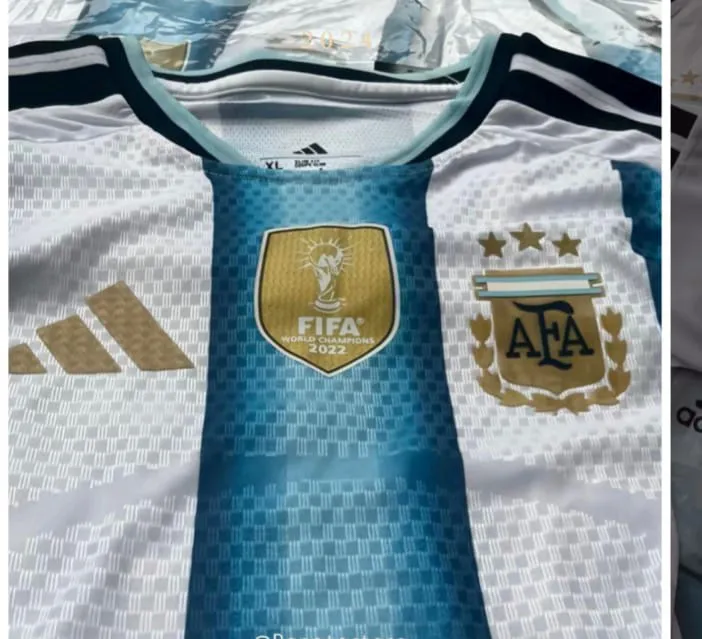 Remera de fútbol blanca con franjas verticales celestes y detalles en dorado. Presenta el escudo de la AFA con tres estrellas y la insignia de "FIFA WORLD CHAMPIONS 2022".