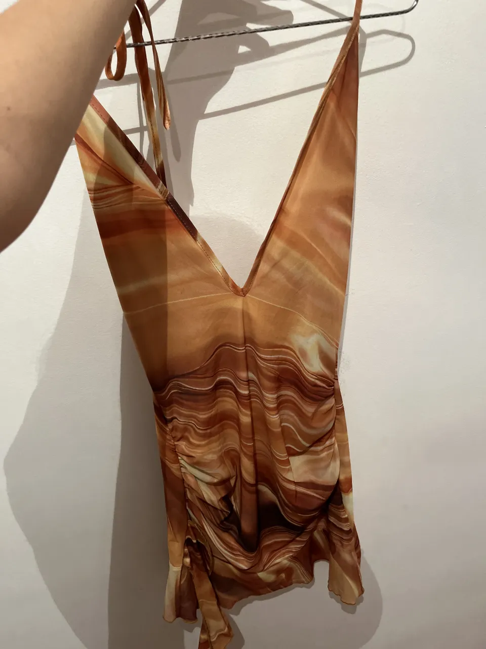 Vestido corto con estampado abstracto en tonos tierra, escote pronunciado en V y detalle de fruncido lateral. Ideal para lucir un look canchero y a la moda.