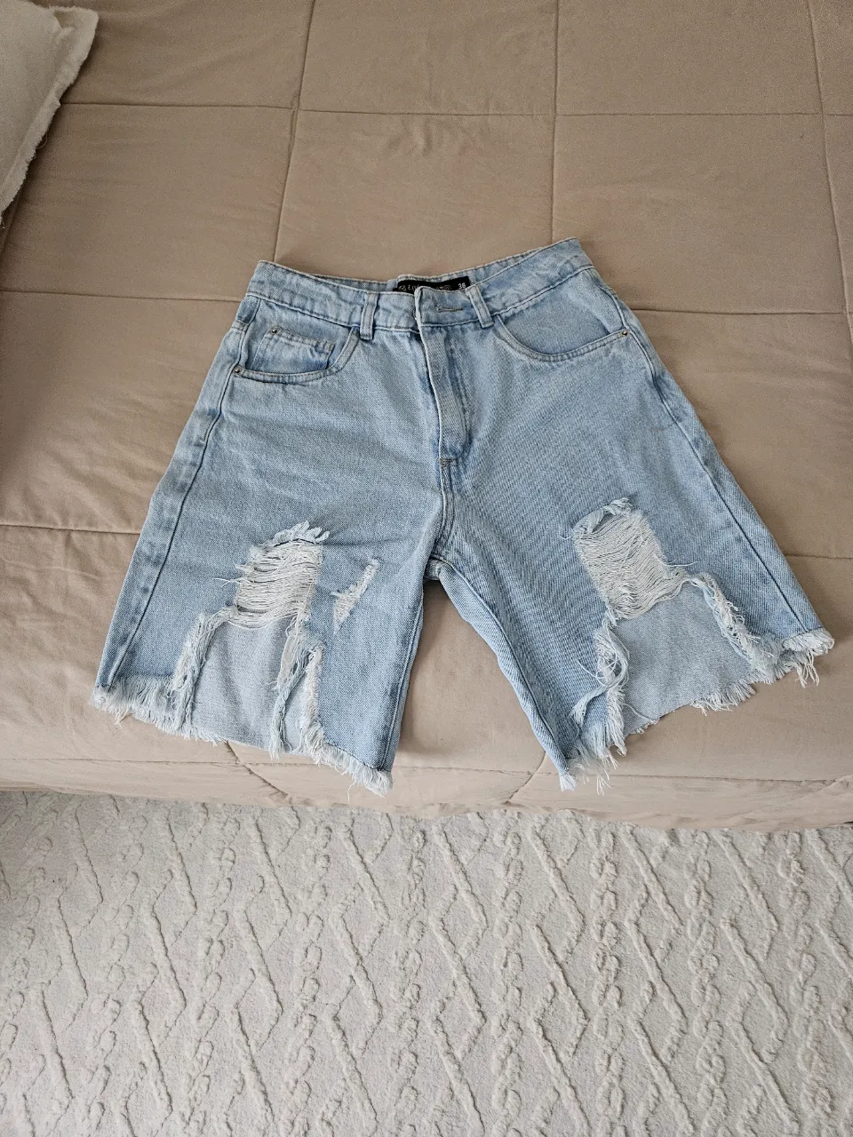 Bermuda de jean celeste con roturas y detalles deshilachados en los bordes inferiores.