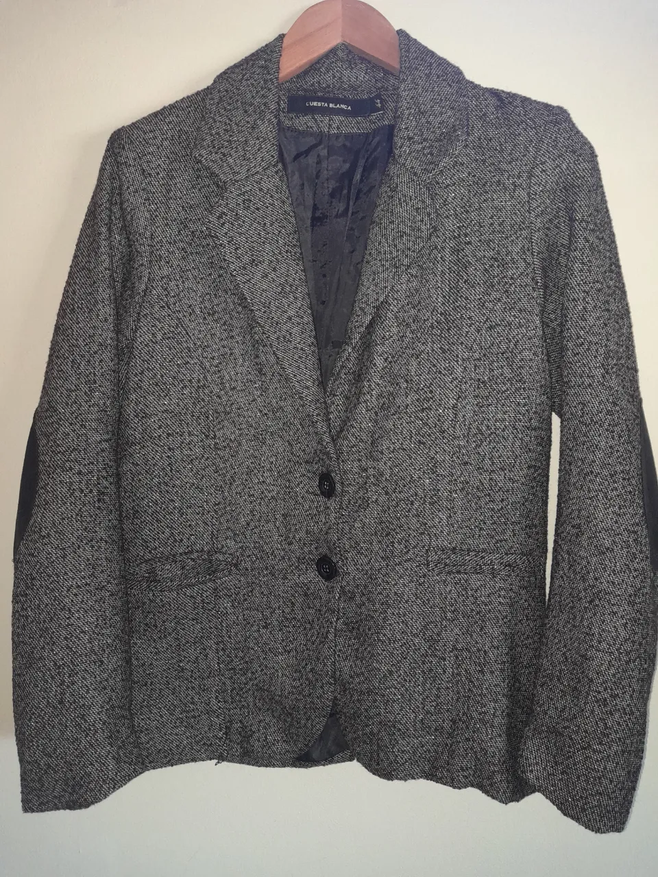 Blazer de tweed gris con parches de cuero en los codos y dos botones al frente.