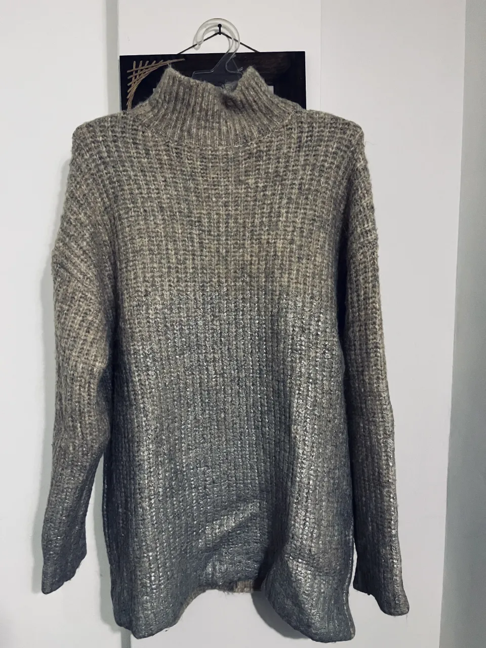 Sweater de tejido grueso con cuello alto. Presenta un degradado de color grisáceo a plateado brillante en la parte inferior.